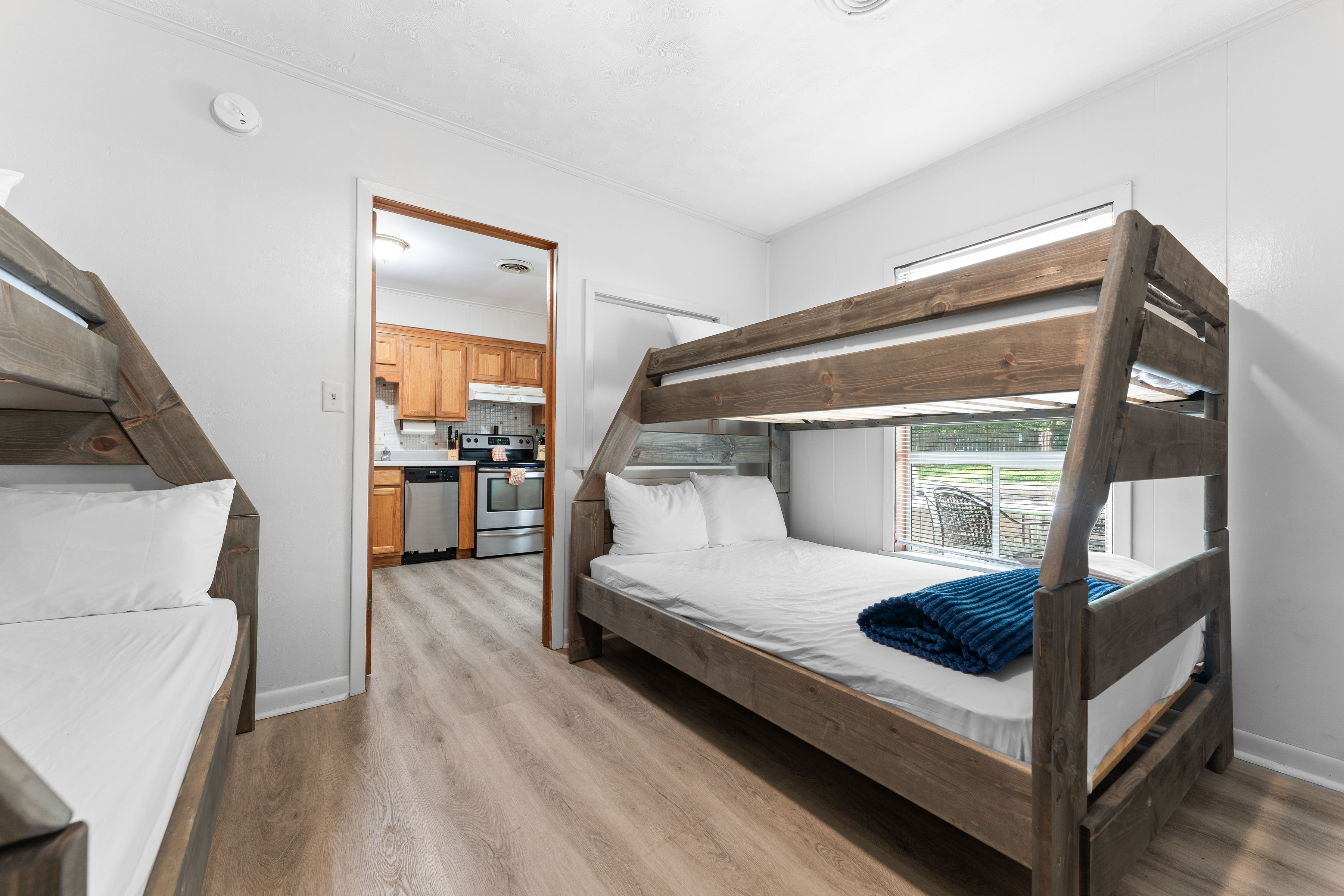 A room with bunk beds and a kitchen in the background.